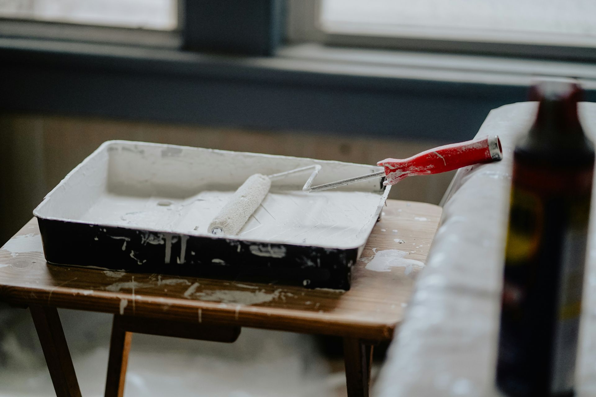 A paint roller with a red handle in a tray of white paint